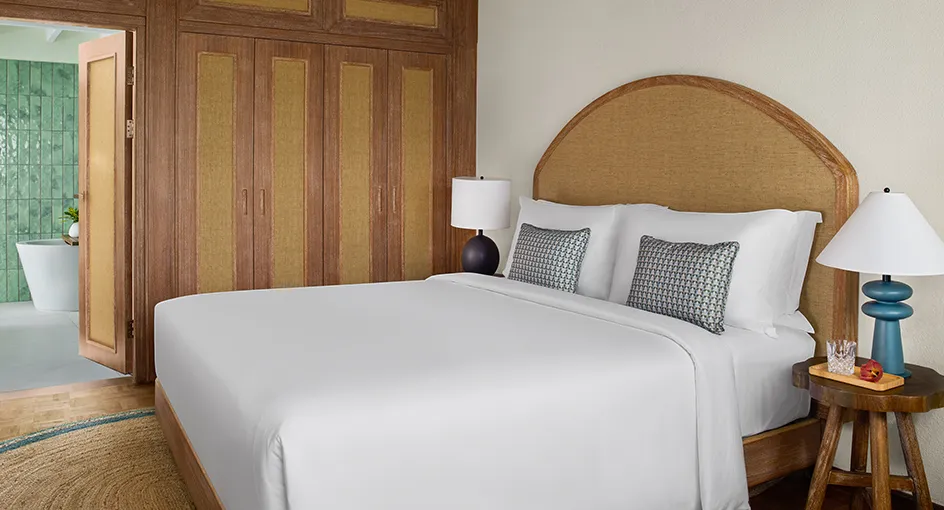 The bedroom of the smallest beach villa: the bed with its rattan headboard, the blue lamps and the timber wardrobe.