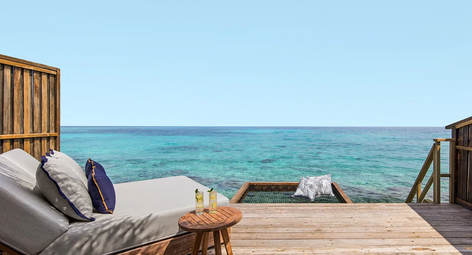 A water villa’s deck: a cushioned lounger, the net stretched over the lagoon and the ladder down to the sea.