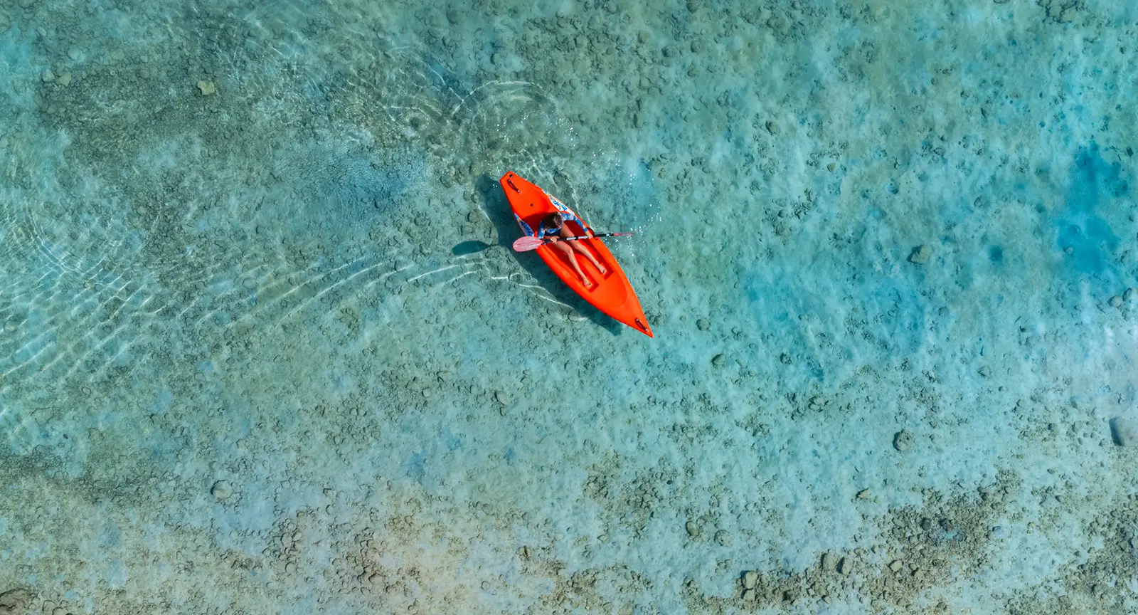 An orange kayak on the clear, shallow lagoon, from above.