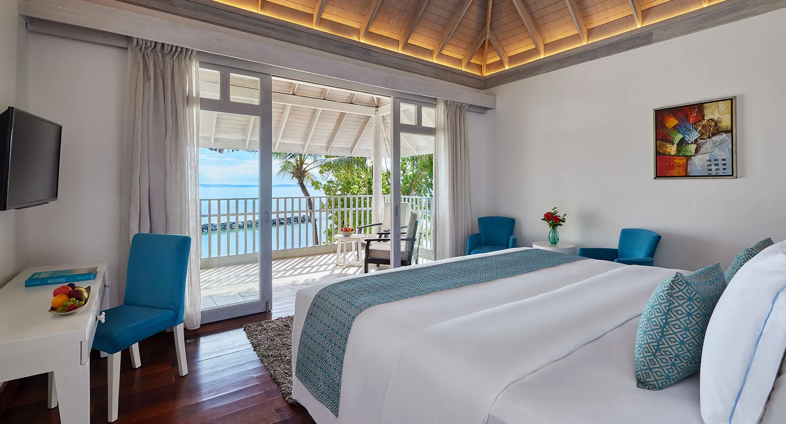 The bedroom of a 2-floor beach suite, with the king bed, the timber ceiling and doors open onto the deck.