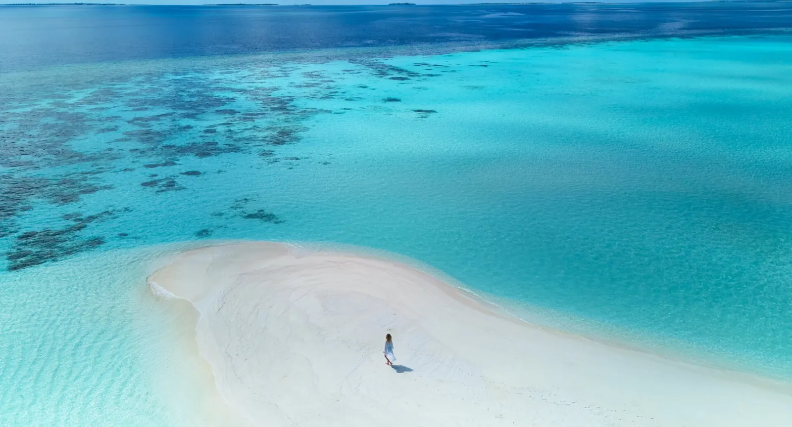 A white sandbank in the middle of the lagoon from above, with one person walking along its edge.