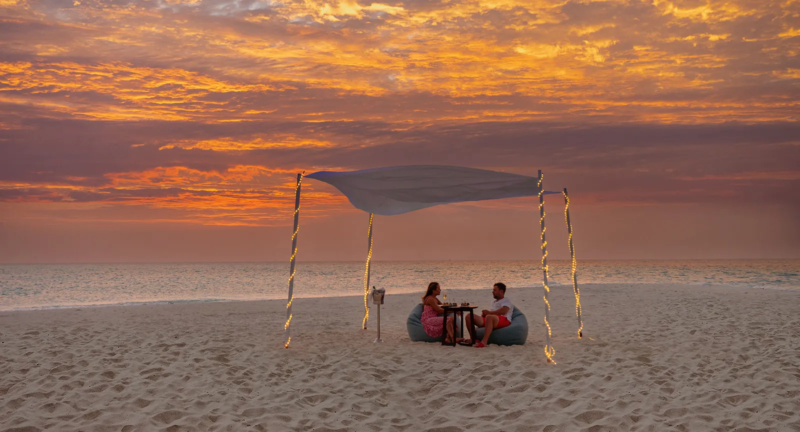 Dinner for 2 on the beach at sunset, under a cloth canopy, the sky turning orange.