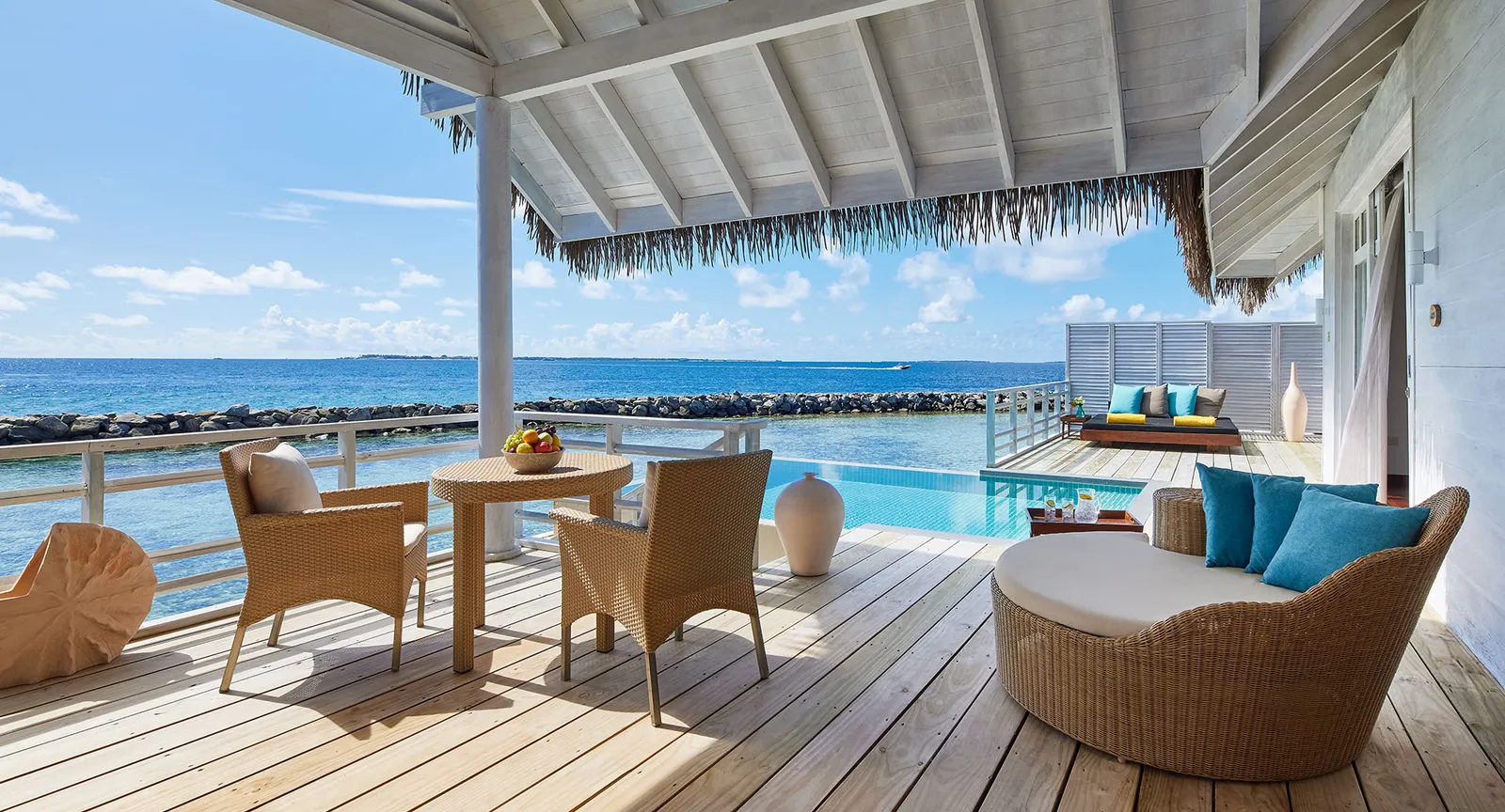The timber deck of a water residence: a table for 2, a round daybed and the private pool facing the sea.