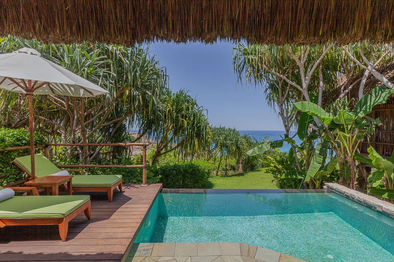 La veranda di Lantoro sotto il tetto di paglia: lettini verdi, la piscina e uno spicchio di mare fra le palme