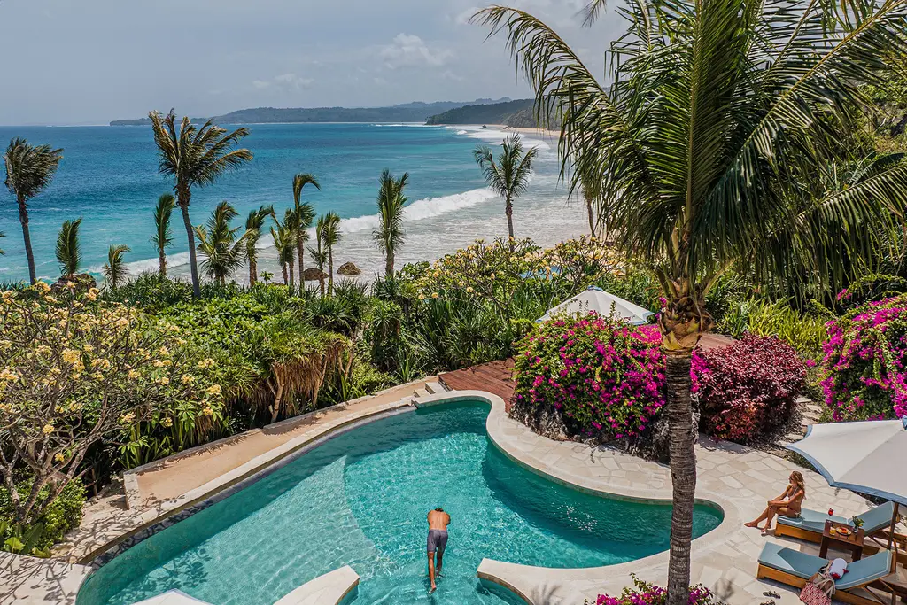 La piscina curva di Putri Wamoro Beach fra i fiori, con la spiaggia di Nihiwatu e le onde in basso