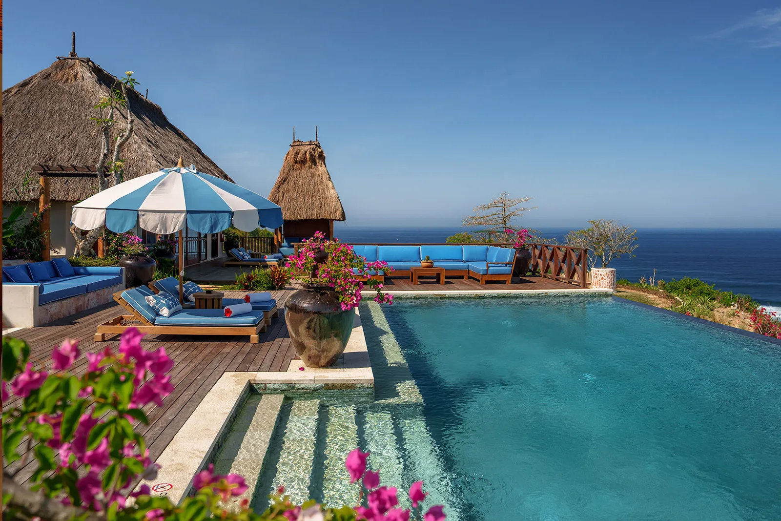 La piscina di Raja Puncak con l’ombrellone a righe, i divani blu e il mare all’orizzonte