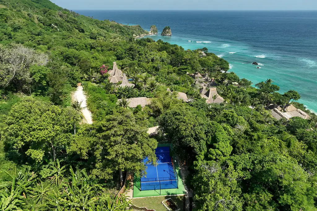 Le ville sulla collina coperta di verde, il campo da padel azzurro in basso e l’oceano dietro
