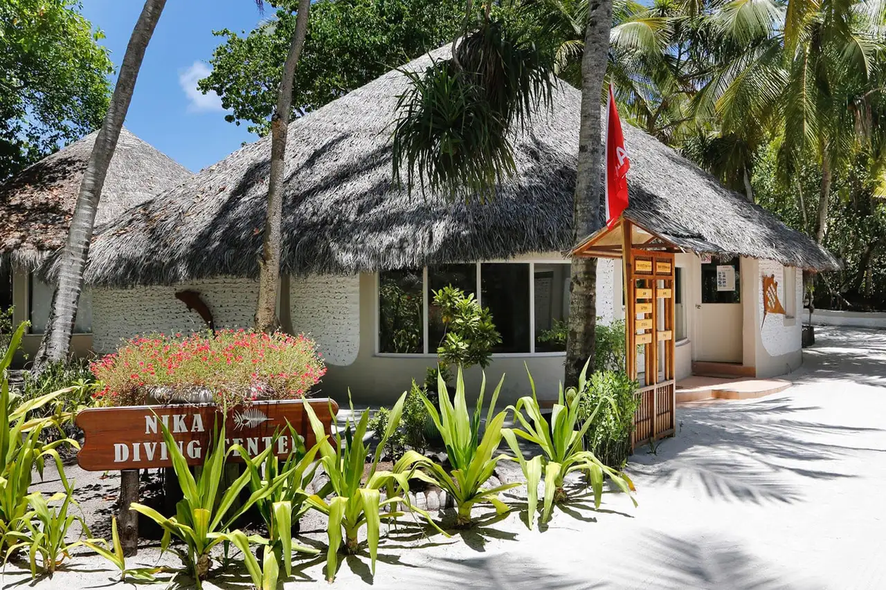 The Nika Diving Center, a thatched hut with its wooden sign and flag among the flowerbeds.