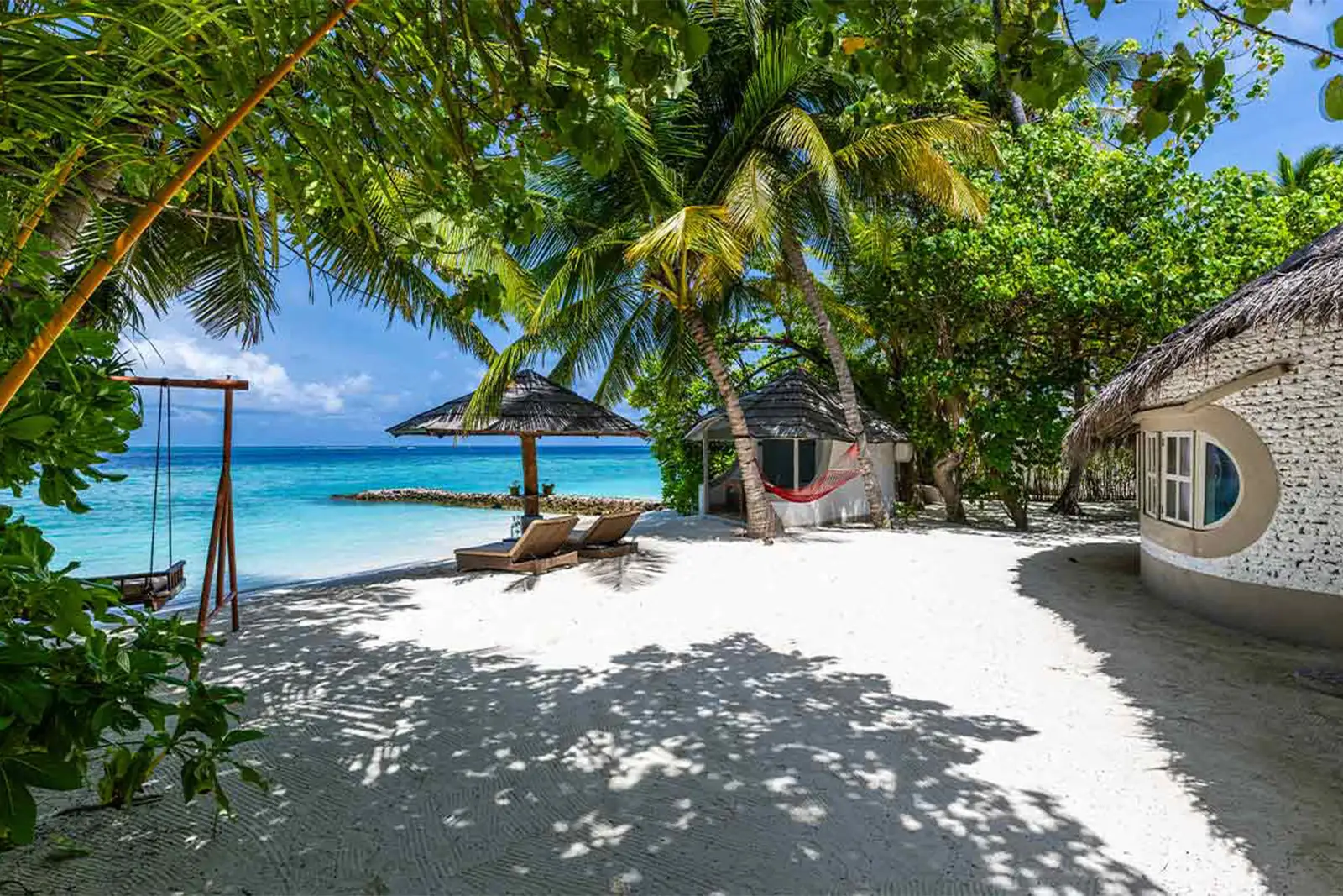 A Beach Villa’s sandy path down to the sea, with a swing hung from a palm.