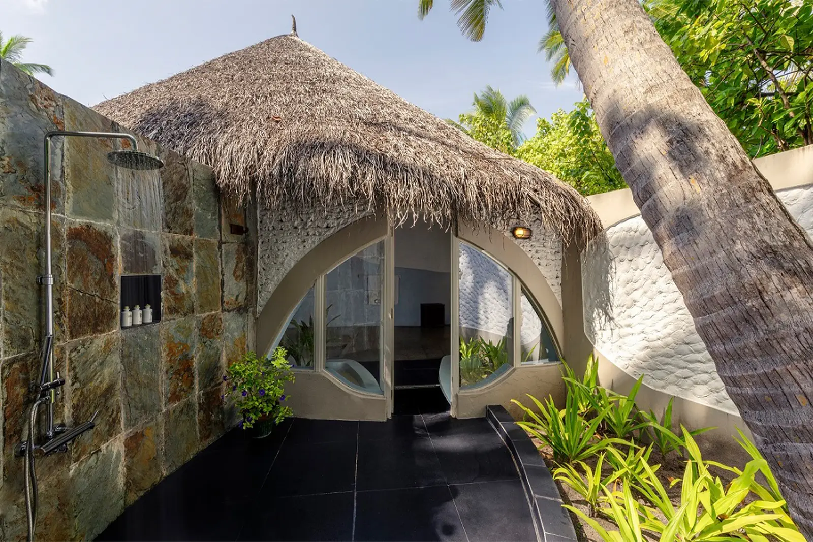A family villa’s open-air shower, with coral walls and plants.