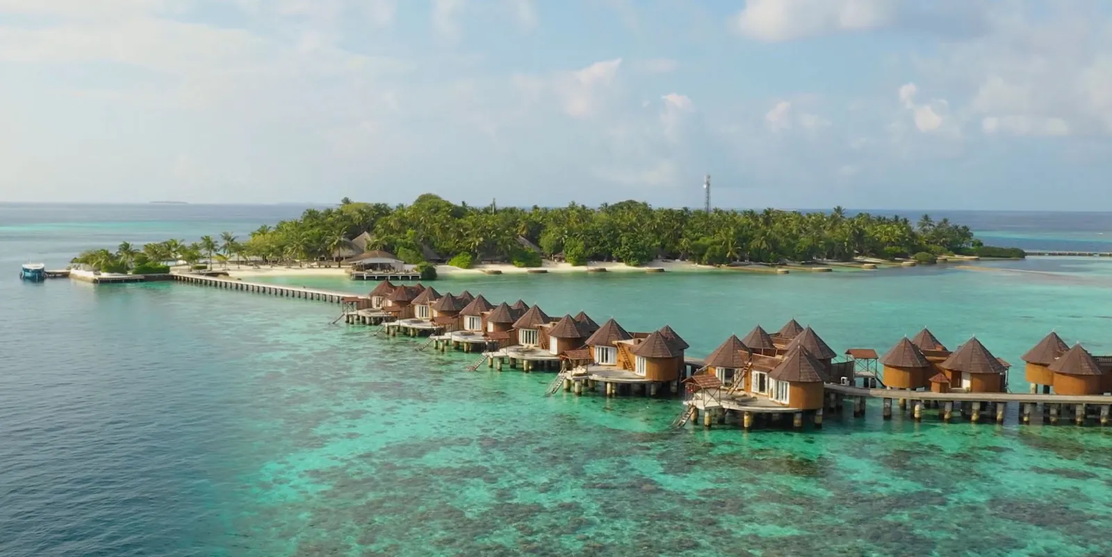 The water villas in a row over the reef, with the walkway tying them to the island and its palms.