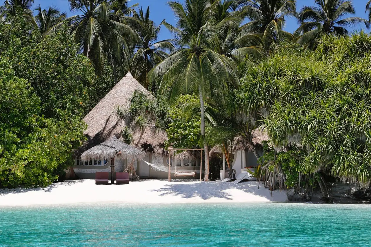 A Beach Villa under thatch among the palms, with its private beach and turquoise water in front.
