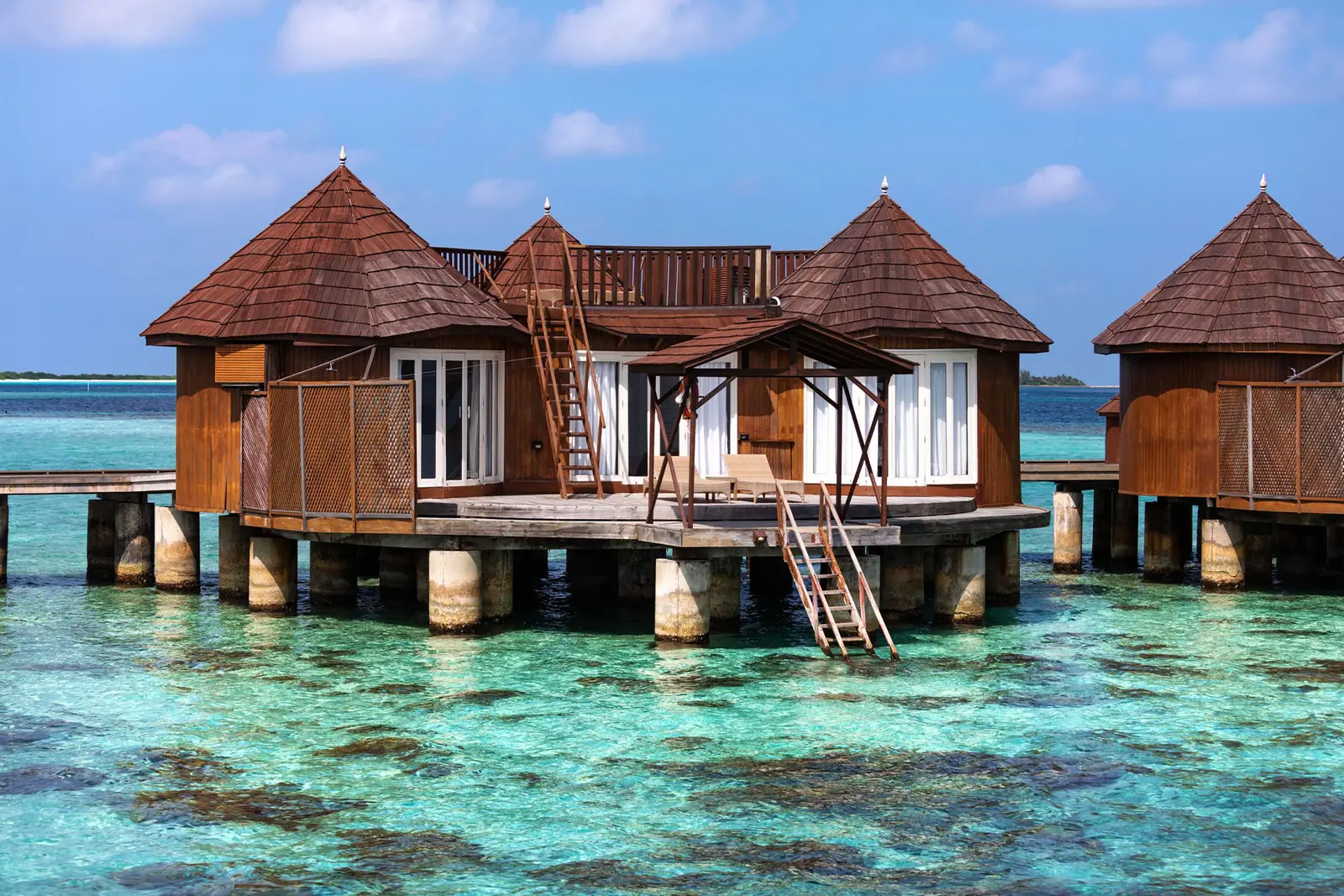 A Family Water Villa on its stilts, with its pointed roof and the reef under the deck.