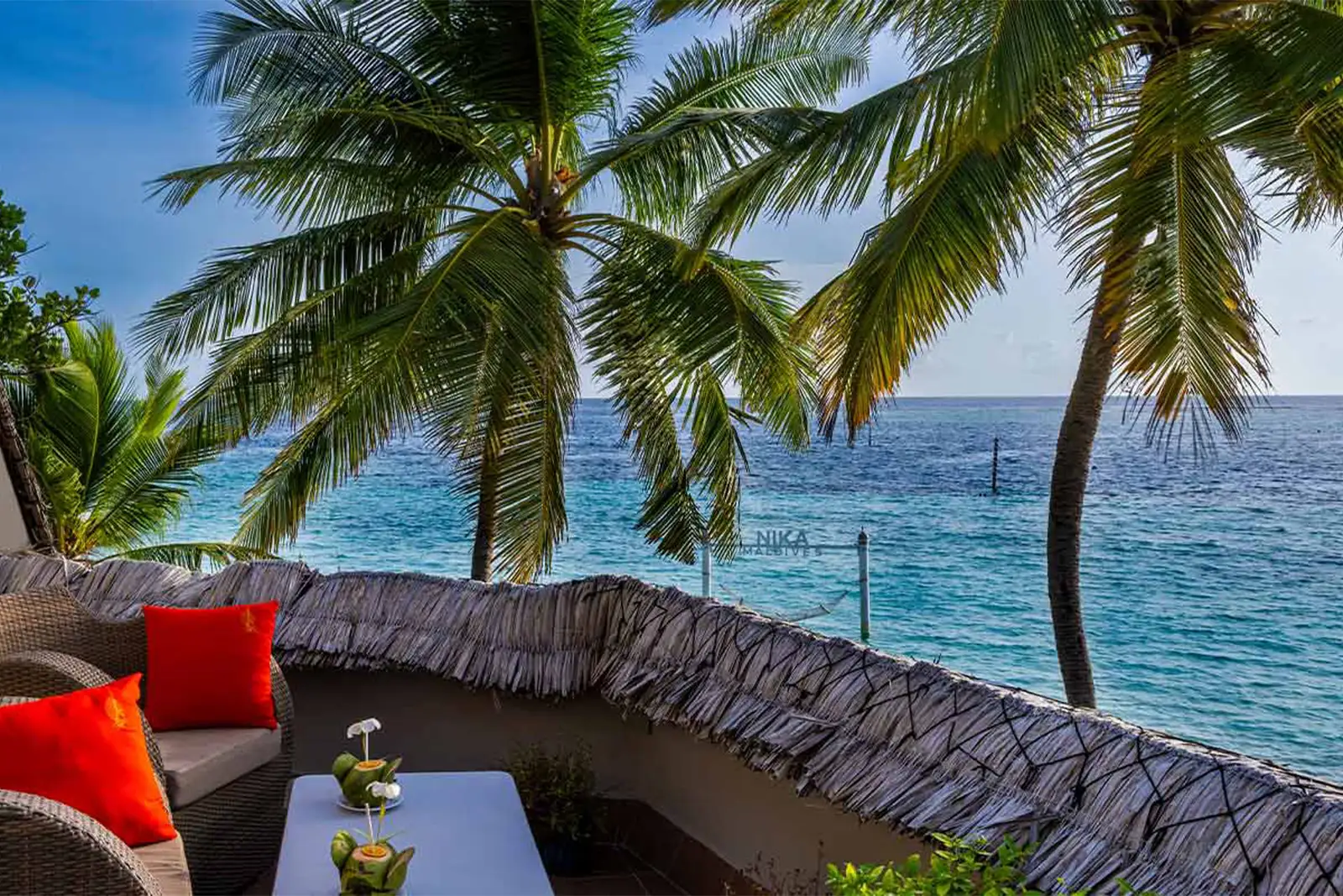 The Faro Studio’s terrace, with red cushions and the open sea between the palms.