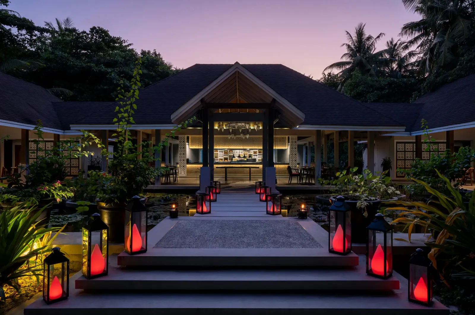 Battuta’s entrance at dusk: red lanterns along the steps and the lit pavilion among the palms.