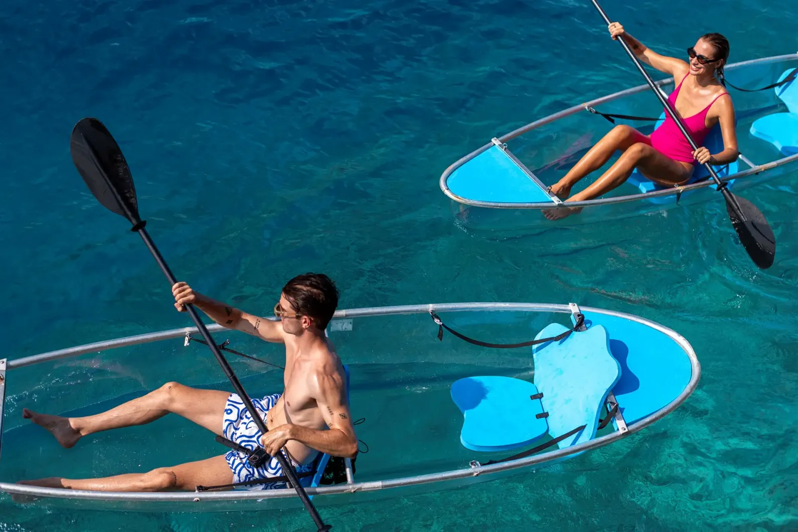 2 guests in glass kayaks on the turquoise lagoon.