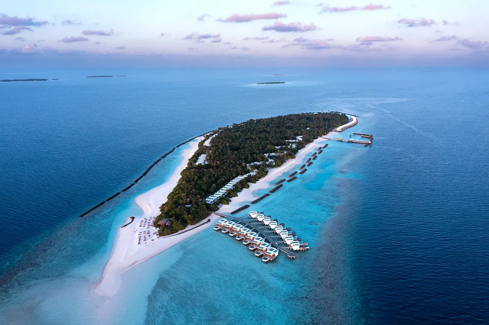 Dhigali from above: the jungle-covered island, the sand spit to the west, the water villas and the reef all around.