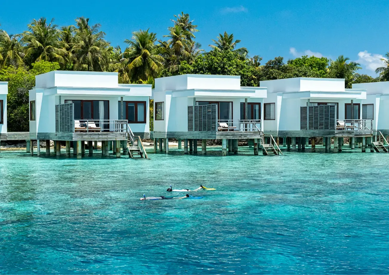 Guests snorkelling on the reef in front of the water villas, in the turquoise lagoon.