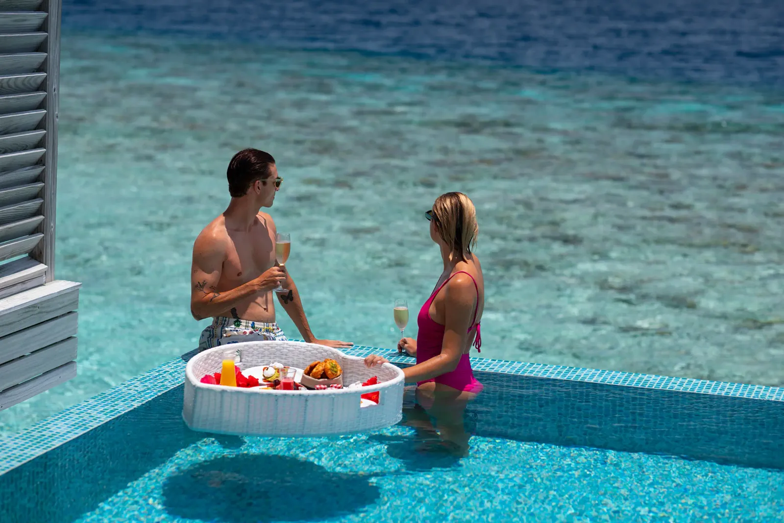A couple in the pool with a floating breakfast tray, on a Lagoon Villa’s deck.