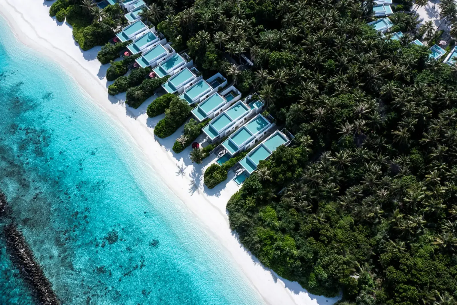 The north shore from above: pool villas in the jungle, the white beach and the rock breakwater in the water.