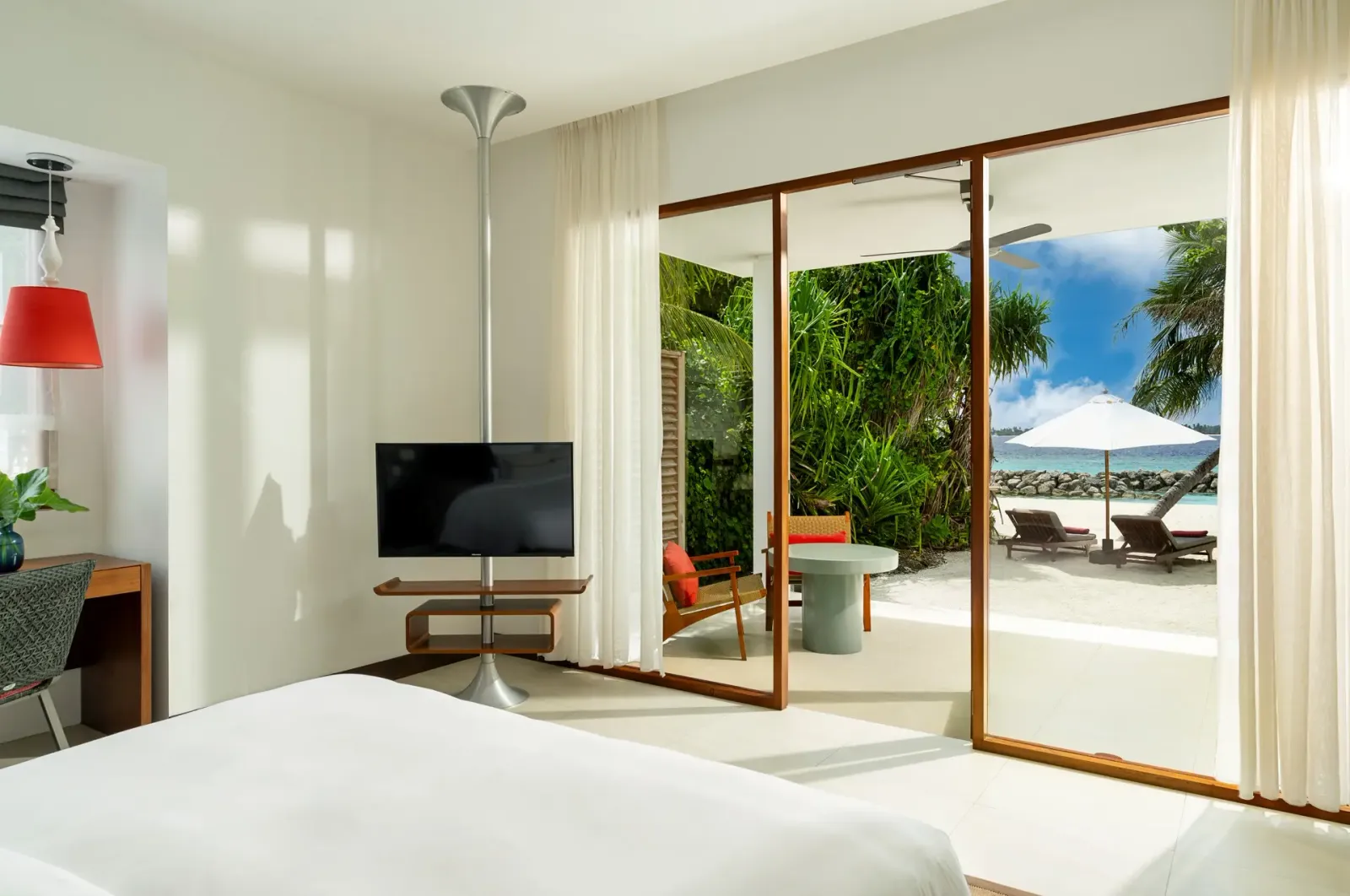 A Beach Bungalow: the bed, the glass doors open to the veranda and the parasols on the beach beyond the plants.