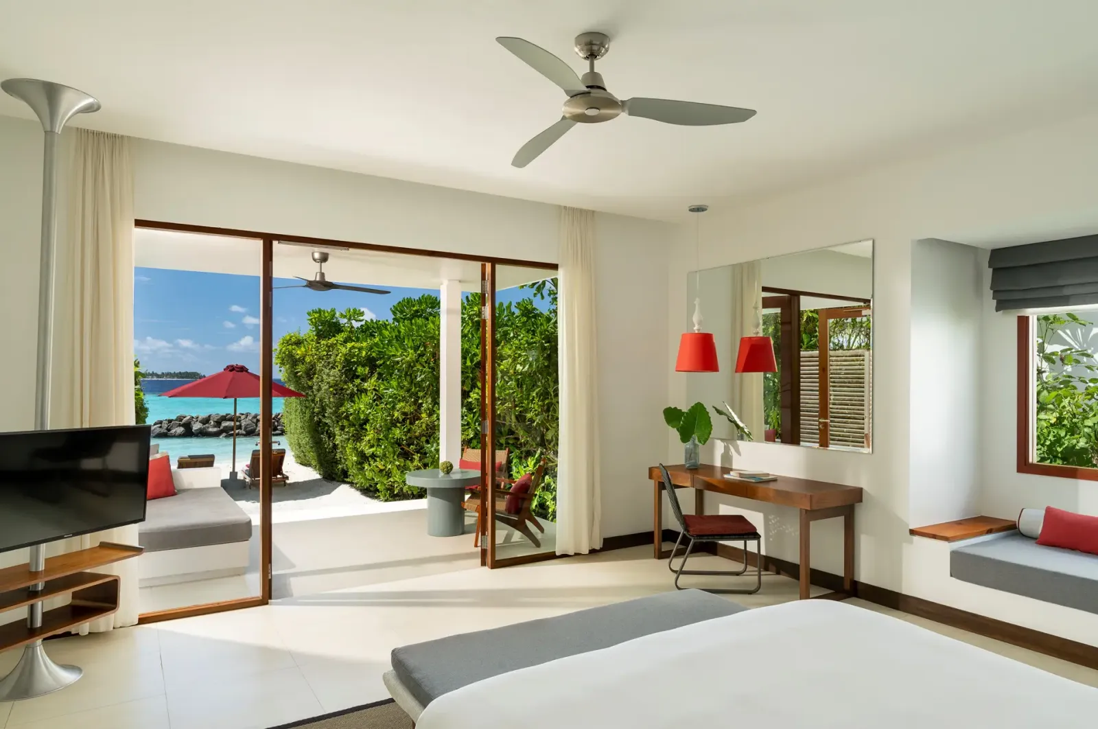 A Beach Villa: the bed, the desk and the glass doors on to the veranda with its red parasol and the sea.