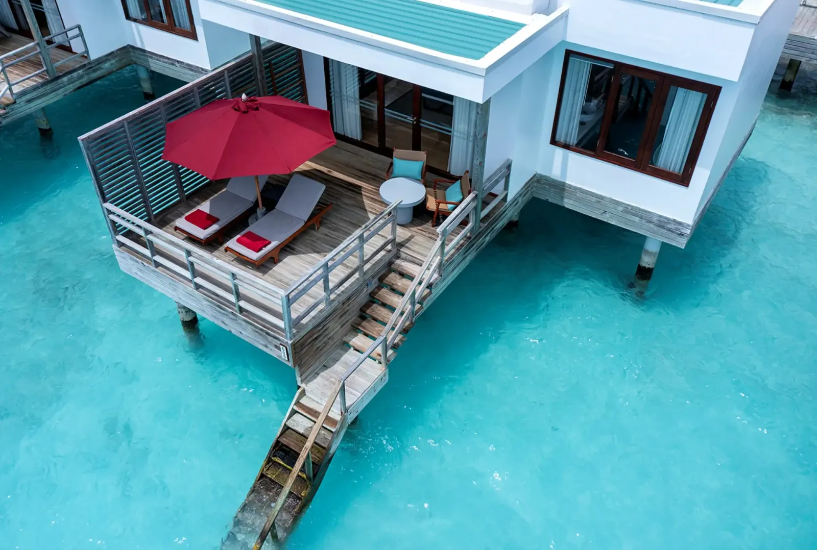 A Water Villa from above: the deck over the water with loungers, a parasol and the steps down into the lagoon.