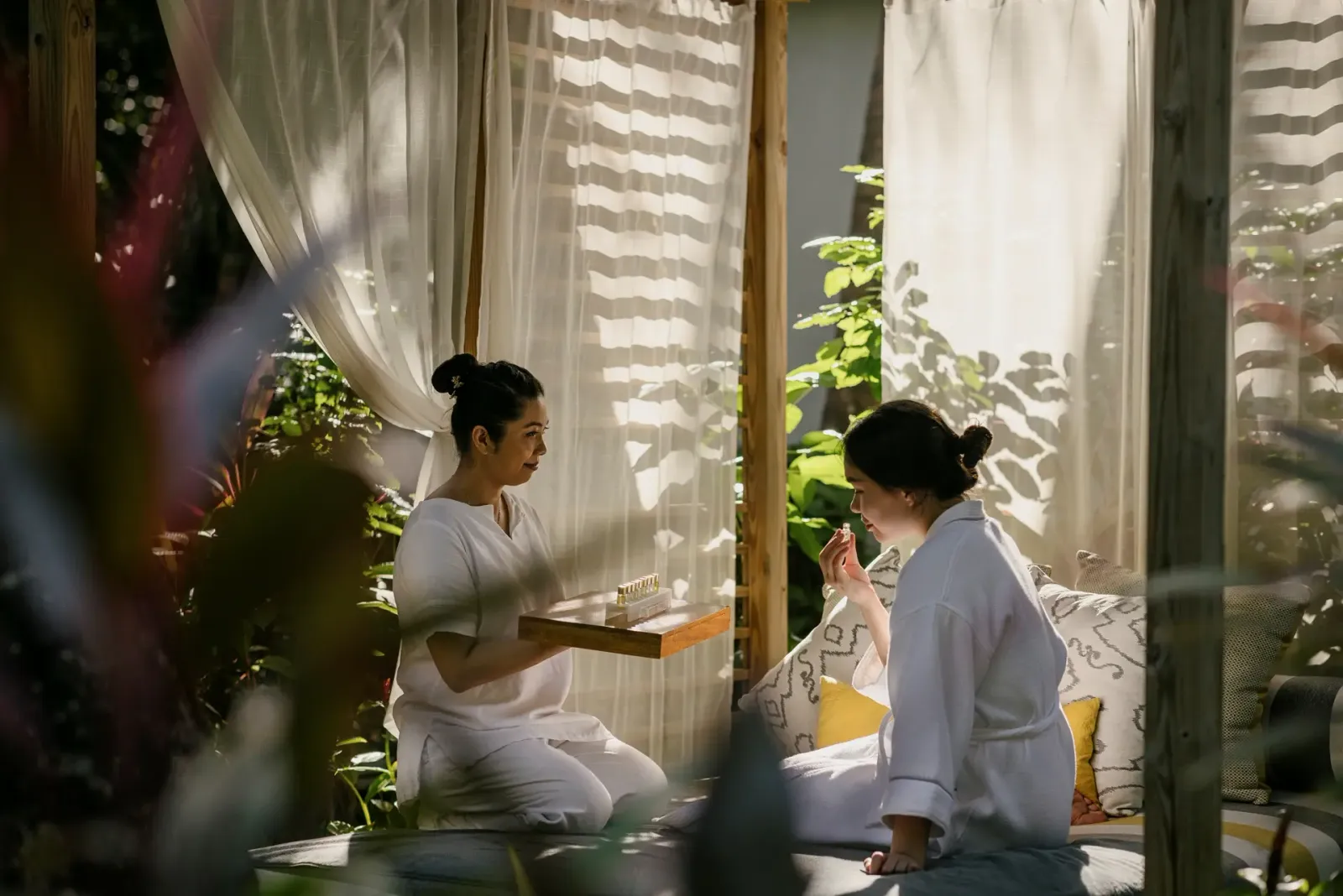 An open-air spa cabana among the plants: a therapist prepares the oils for a guest in a robe.