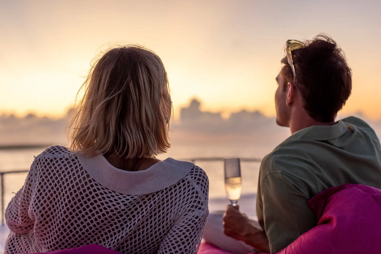 A couple with glasses of sparkling wine on the sunset cruise boat, an orange sky on the horizon.