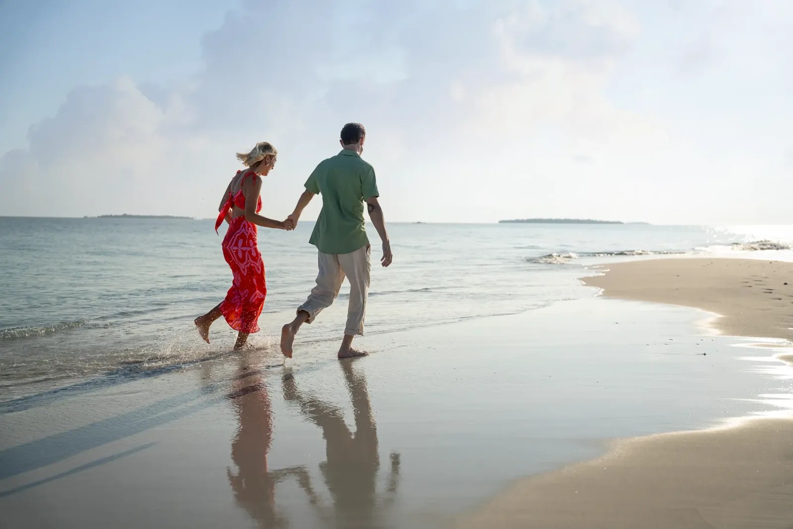 A couple walking hand in hand along the sand spit, feet in the shallow water.