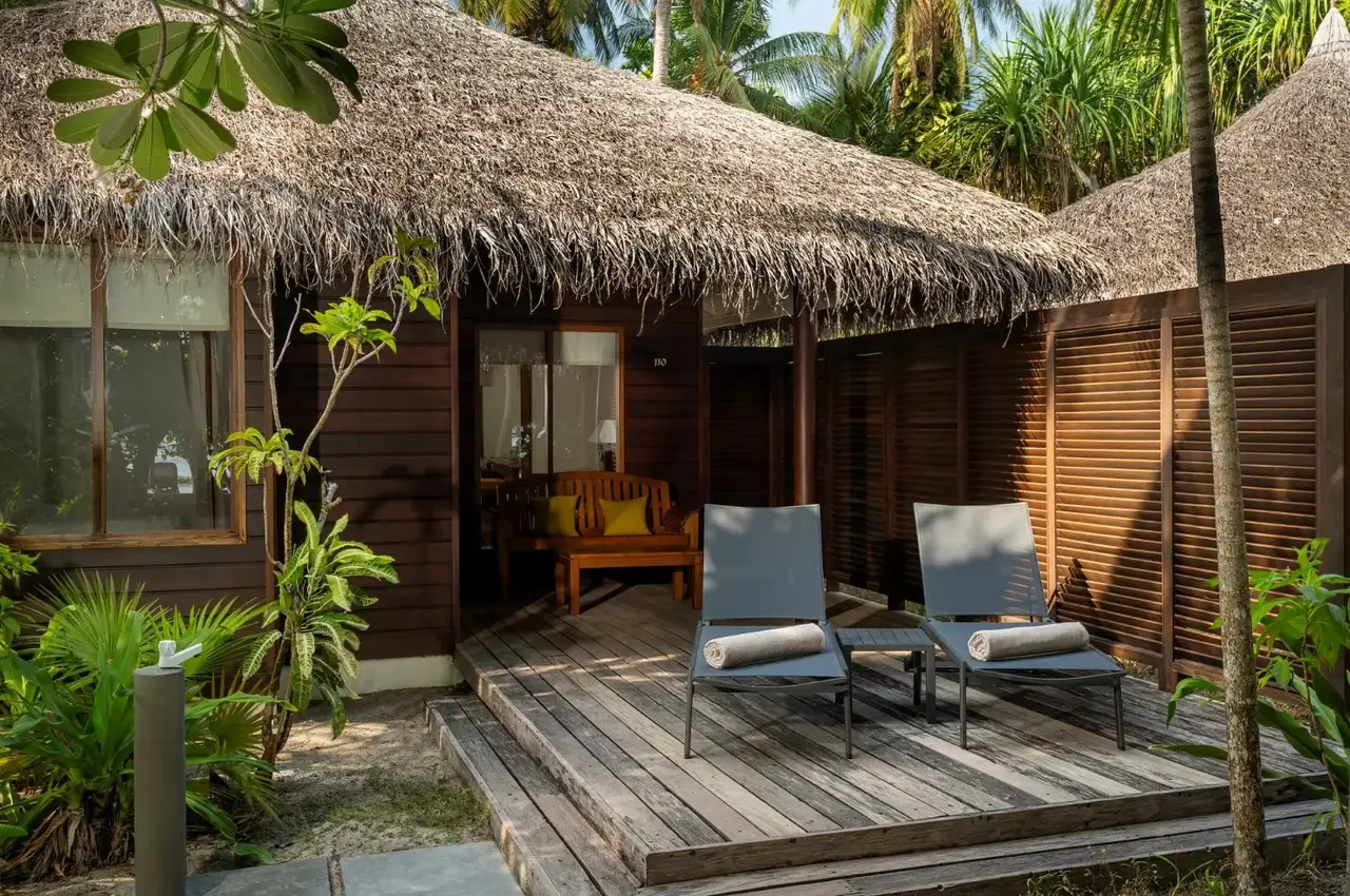 The deck of a dark-timbered Beach Bungalow, 2 loungers among the garden plants