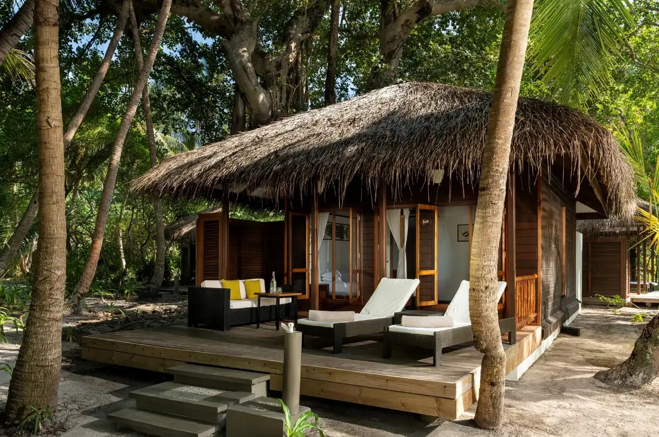 A thatched Beach Villa among the trees, with its timber deck and 2 loungers