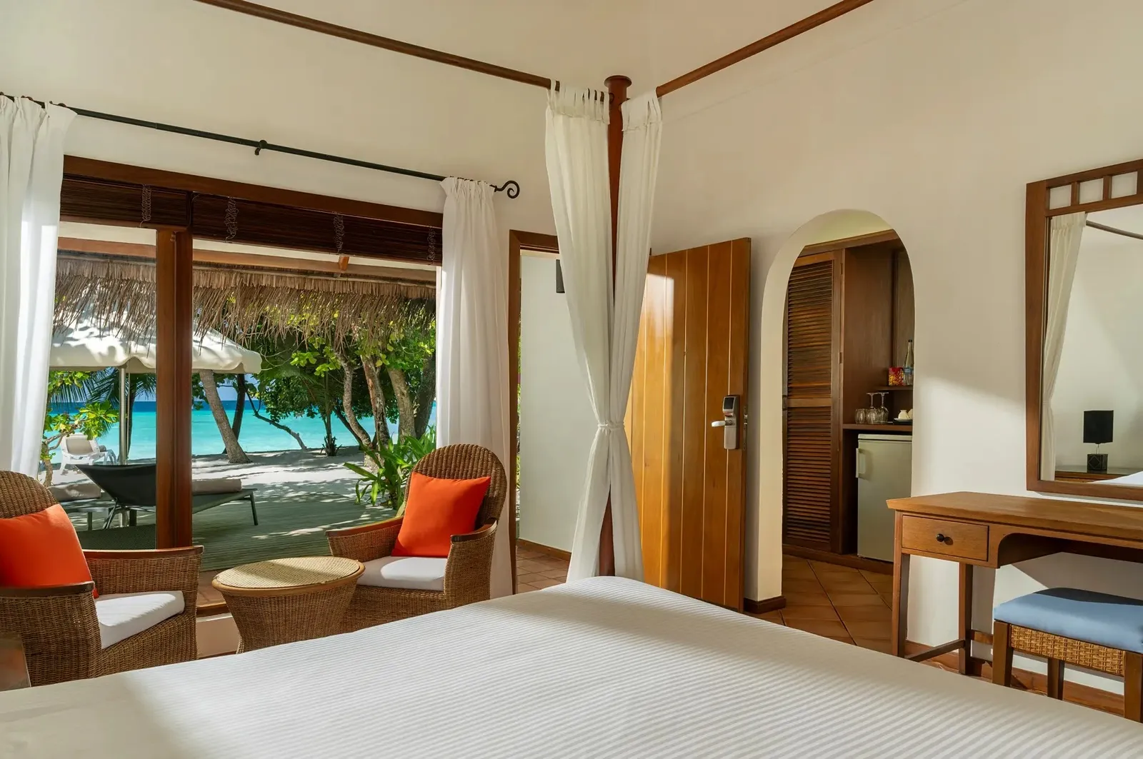 A Deluxe Beach Villa’s bedroom, the four-poster’s drapes and the lagoon beyond the deck