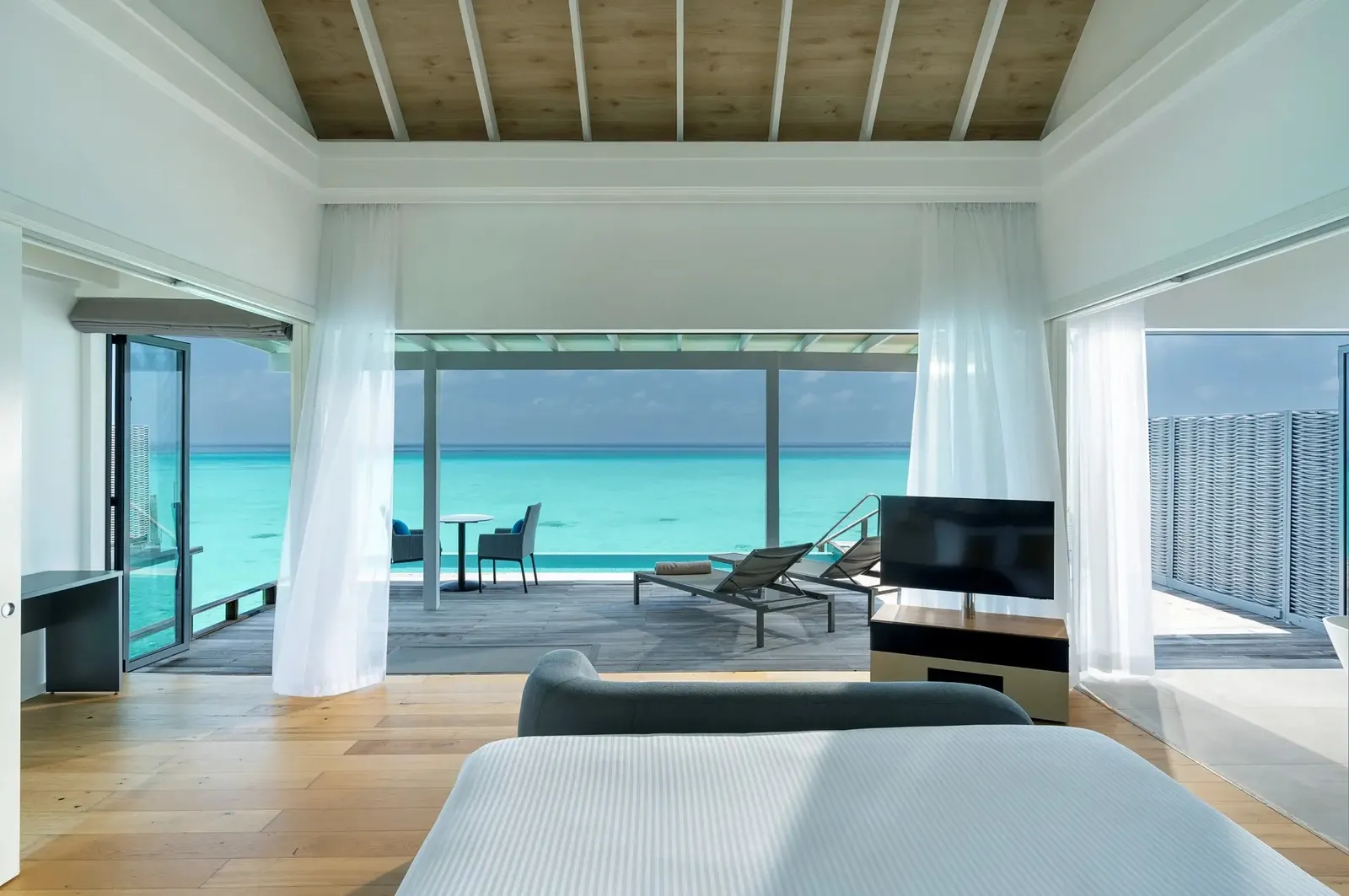 A Water Villa with Pool’s bedroom, the bed and the glass doors open onto the deck and the lagoon