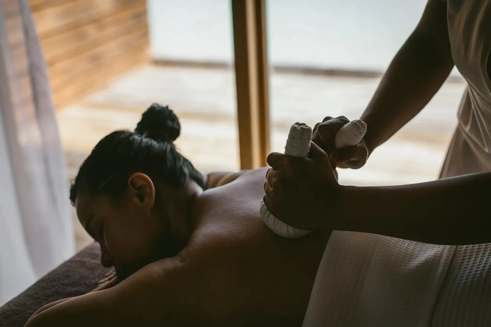 A massage with warm herbal compresses on the back, in the half-light of a spa room