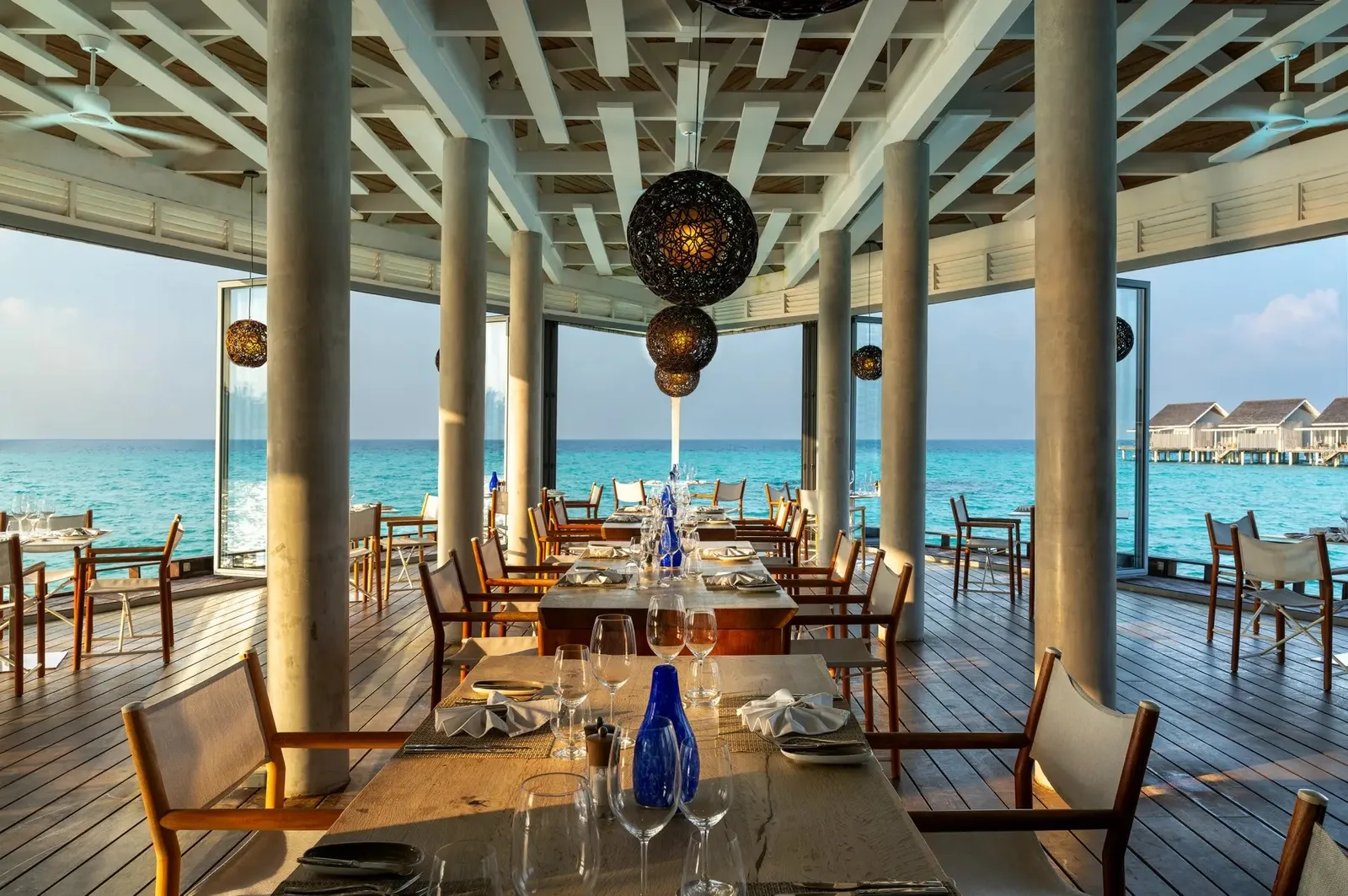 The Reef’s dining room open to the sea, tables laid and the water villas on the horizon