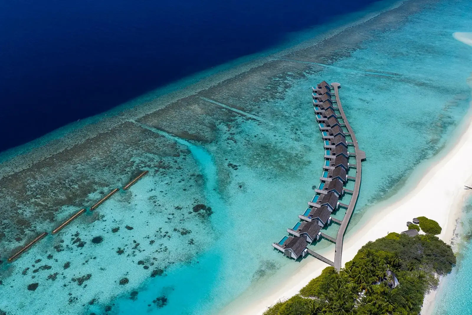 The water villas along a curving jetty, seen from above over the reef and the lagoon