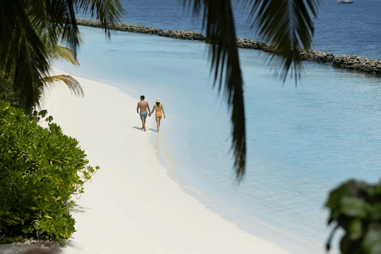 A couple on the white beach, the turquoise lagoon and the palms