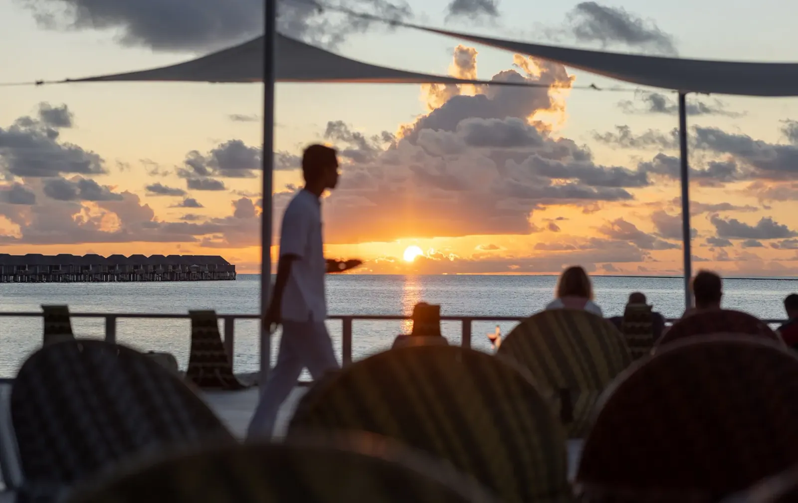 Il Chill Bar al tramonto: un cameriere fra i tavoli, il sole che cala dietro le ville sull’acqua.