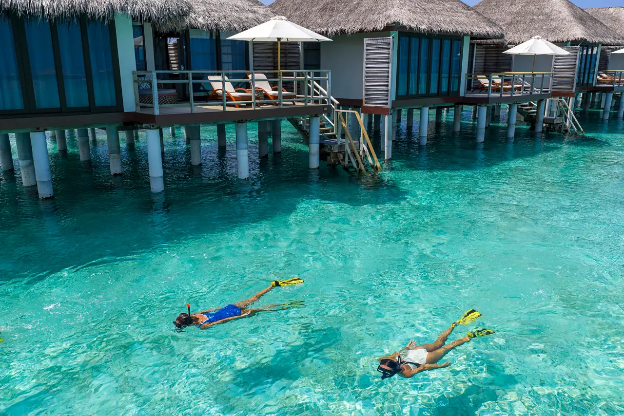 2 persone fanno snorkelling nella laguna chiara davanti alle ville sull’acqua con la scaletta.