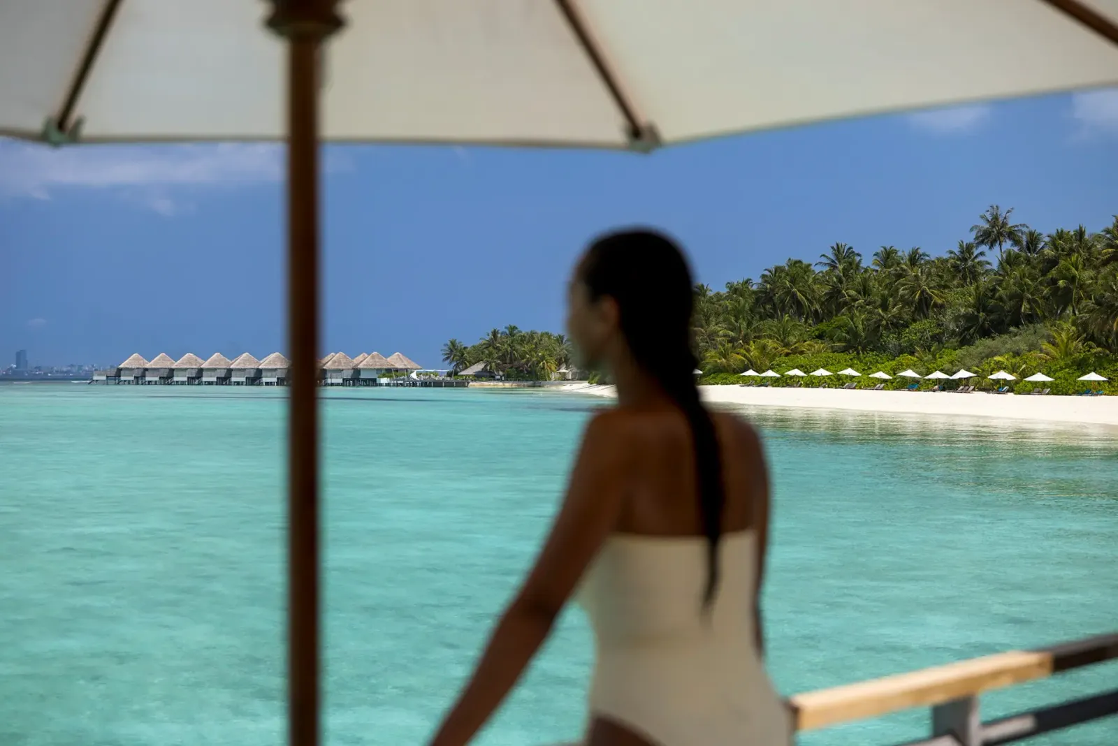 Un’ospite sulla terrazza di una villa sull’acqua guarda la laguna; in fondo la fila delle ville e la spiaggia con gli ombrelloni.