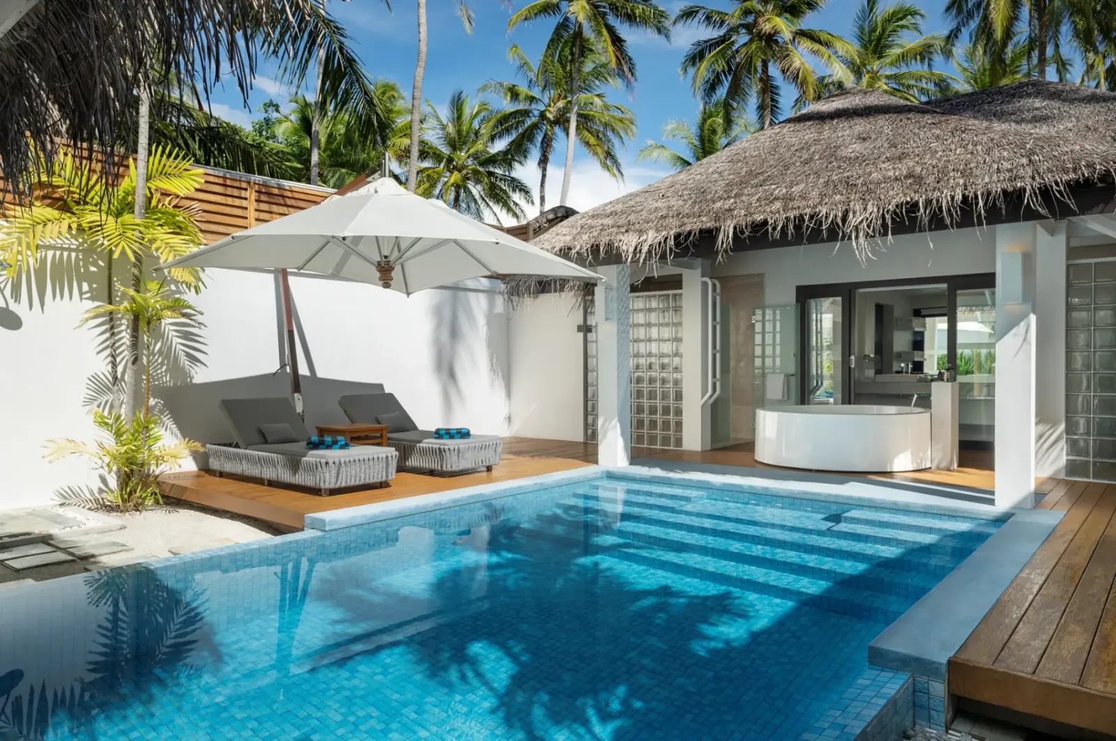 La Pool Villa: la piscina fra le palme, i lettini e la vasca da bagno all’aperto sotto il tetto di paglia.