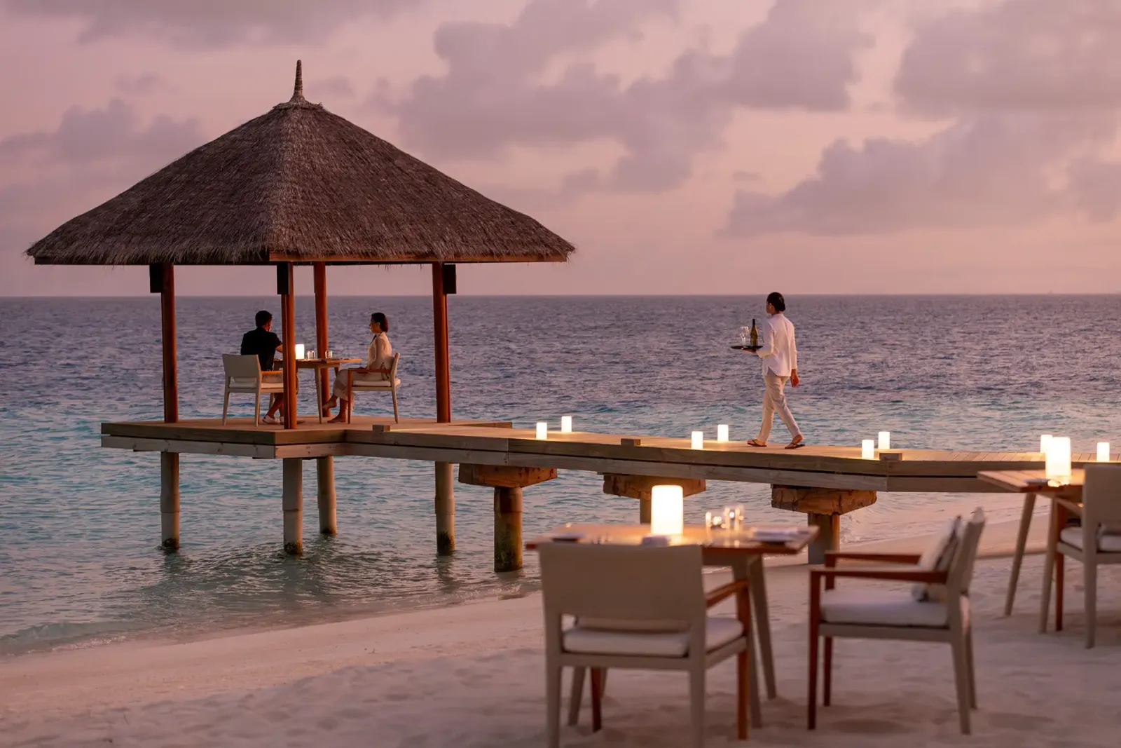Una cena sulla piattaforma di Sand all’imbrunire: un padiglione di paglia sull’acqua, le candele sul pontile e i tavoli sulla sabbia.
