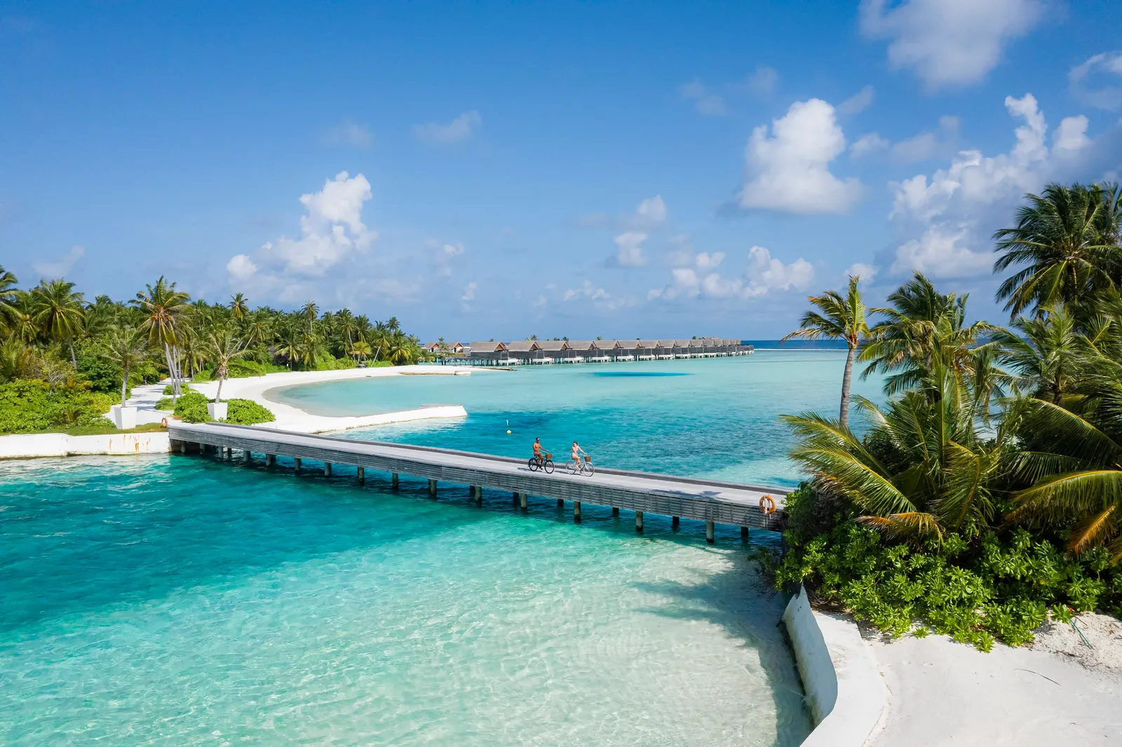2 guests cycling over the bridge linking the 2 islands, above turquoise water