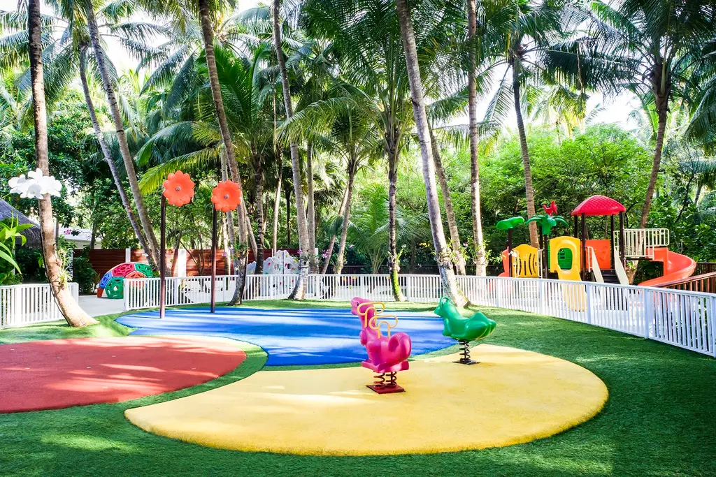 The kids’ club garden, with its slide, play equipment and coloured lawn among the palms