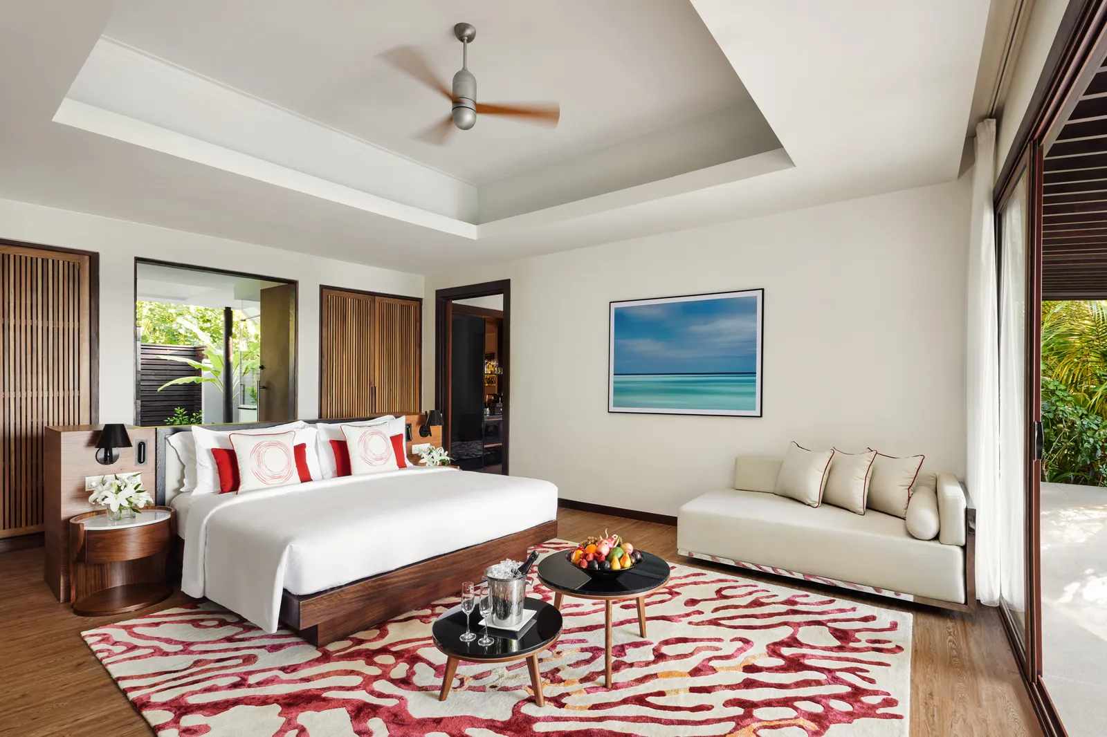 The bedroom of a Deluxe Family Beach Pool Villa, with a red rug and the garden outside