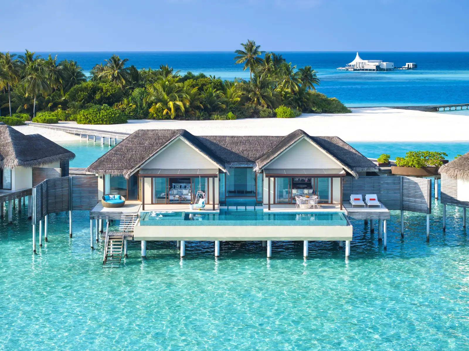 An overwater pavilion with its pool, seen from the lagoon, with Edge in the distance