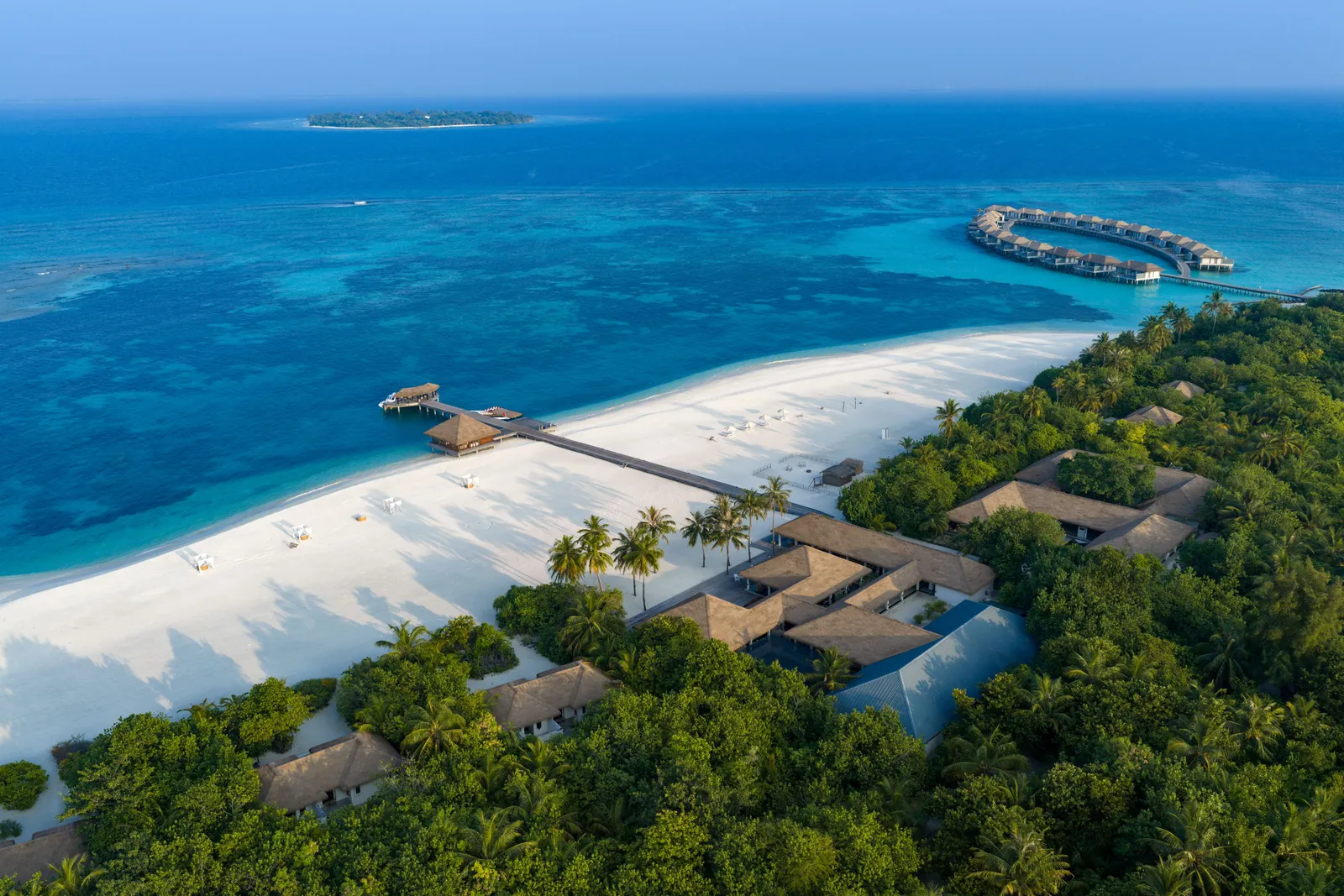 Noku’s wide beach from above, the roofs of the main buildings among the palms and the water villas in the distance.