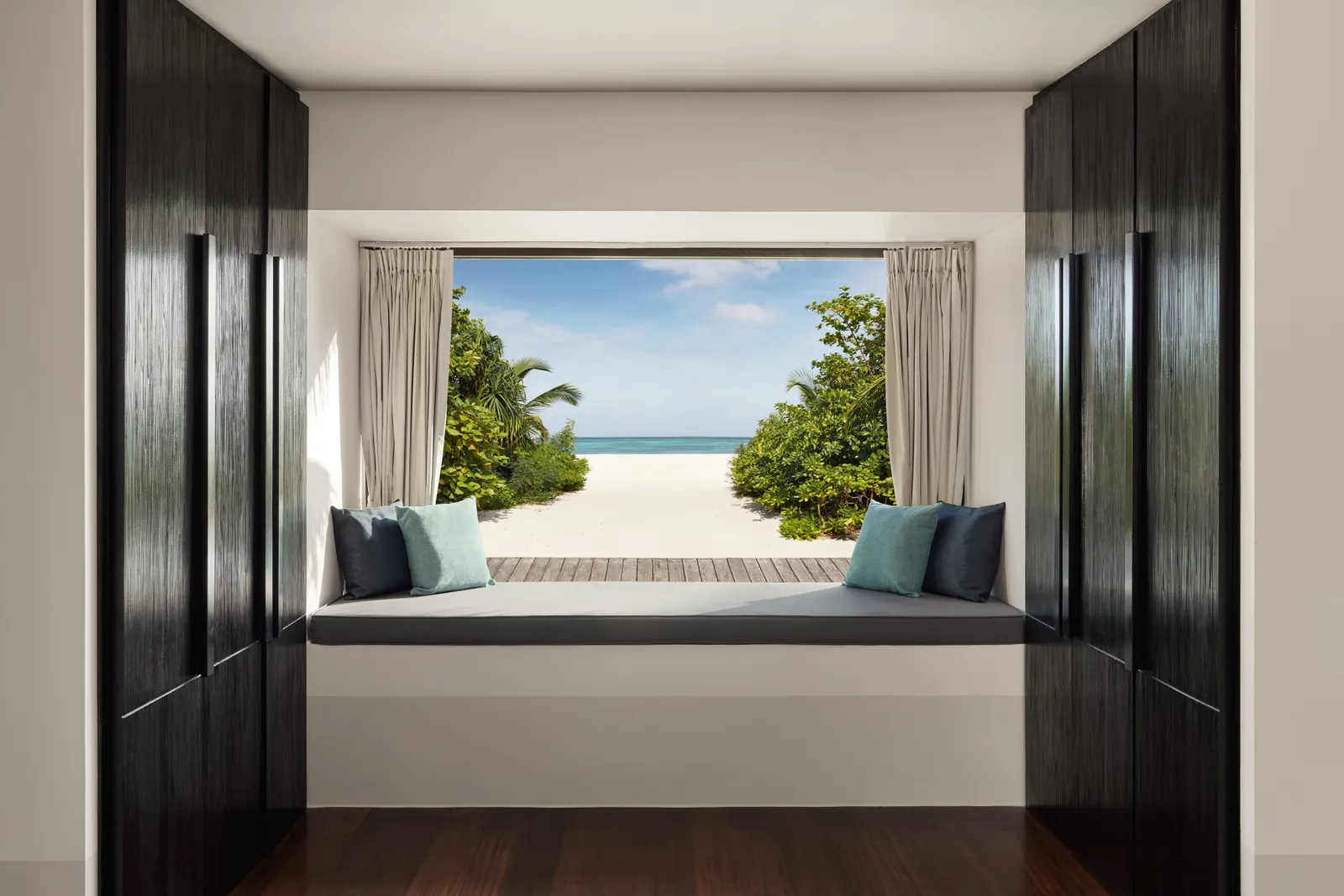 The window seat of a beach villa, framing the sandy path through the green down to the sea.