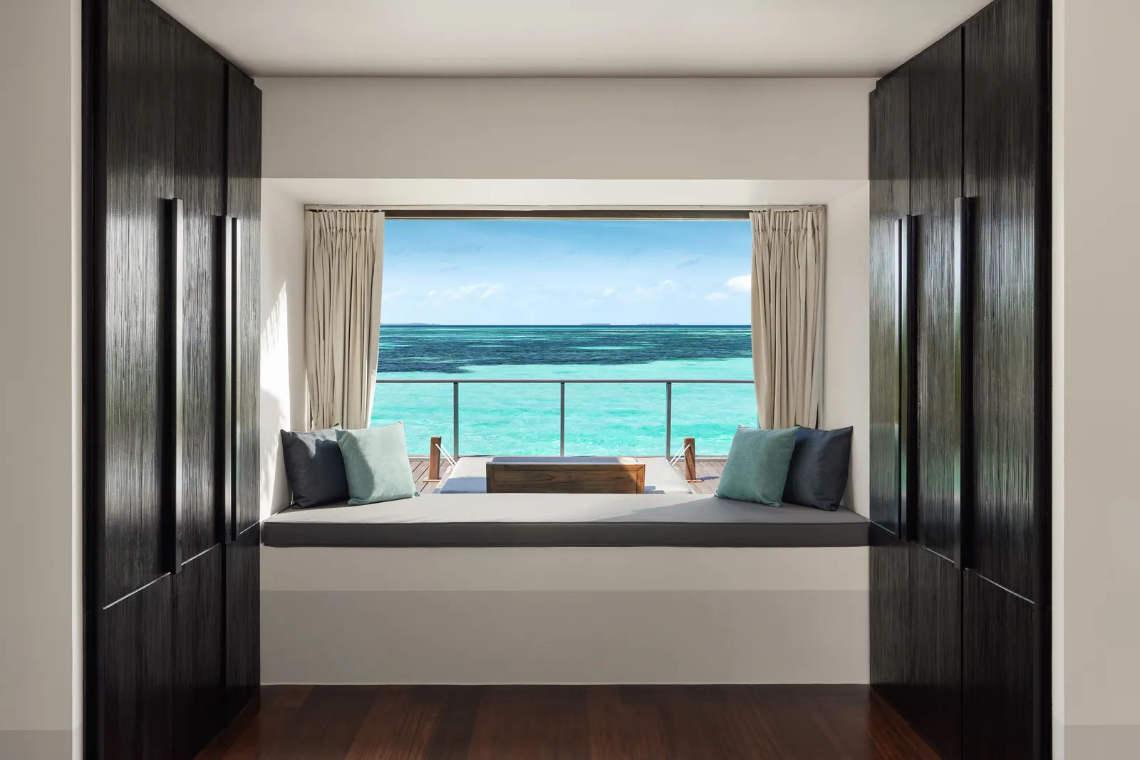 The window seat of a lagoon-view water villa, open onto the deck and the turquoise sea.